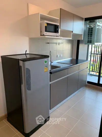 Modern kitchen with sleek cabinets, fridge, and microwave in a bright apartment.