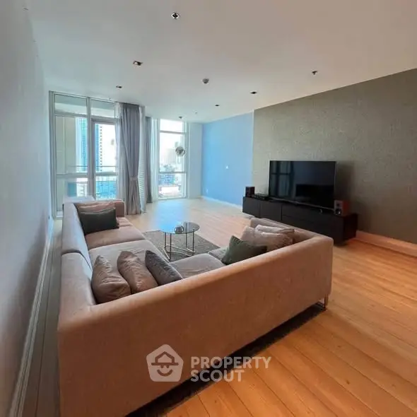 Spacious modern living room with large windows and city view, featuring elegant furniture and wooden flooring.