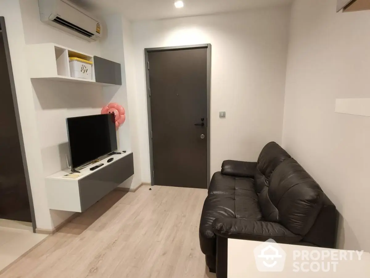 Modern living room with sleek black sofa and wall-mounted TV in minimalist apartment.