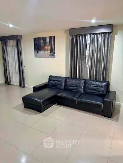Spacious living room with sleek black leather sofa and elegant curtains