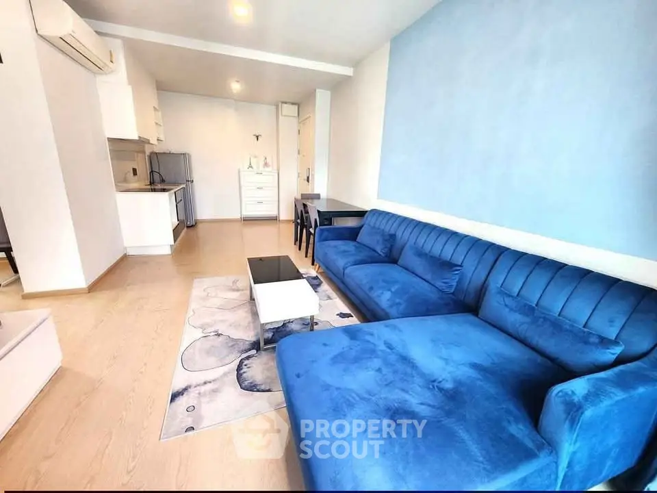 Modern living room with blue sofa and open kitchen layout in stylish apartment.