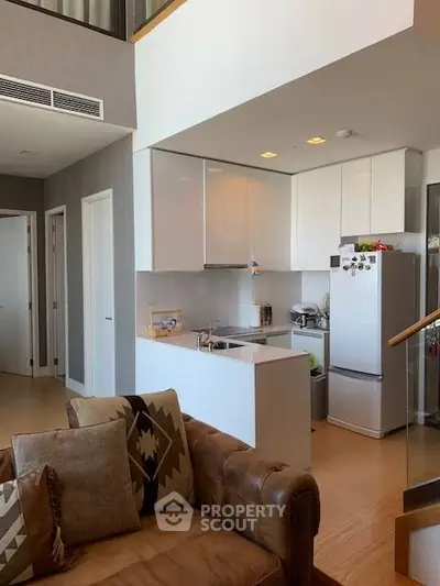 Modern open-layout kitchen with sleek white cabinets and cozy living area in a stylish apartment.