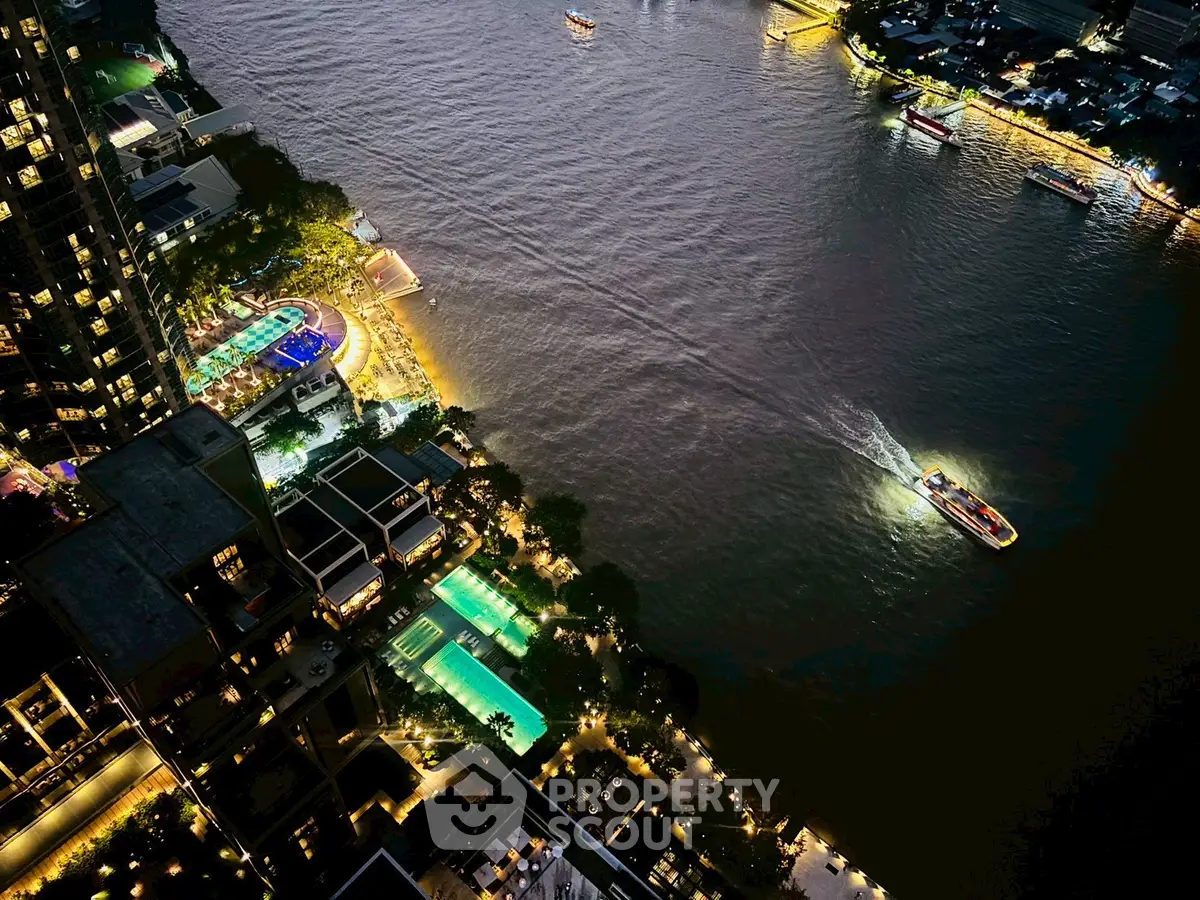 Stunning aerial view of riverside luxury apartments with illuminated pools and vibrant cityscape at night.