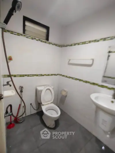 Compact bathroom with essential fixtures and tiled walls, featuring a toilet, sink, and showerhead.