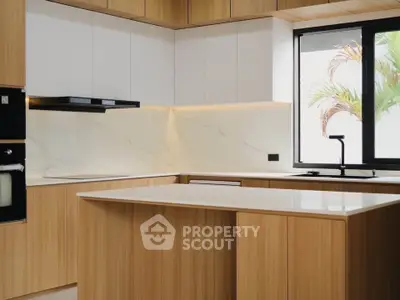 Modern kitchen with sleek wooden cabinetry and marble countertops, featuring a large window and built-in appliances.