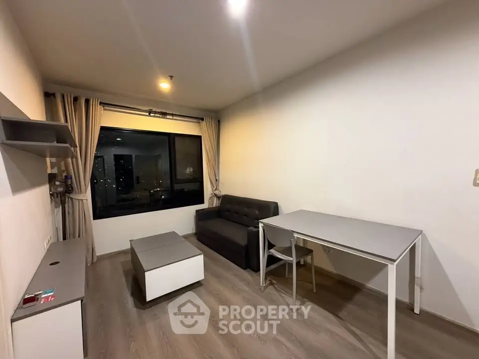 Modern living room with sleek furniture and large window offering city views.