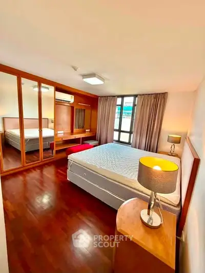 Spacious bedroom with wooden flooring and large mirrored wardrobe in modern apartment.
