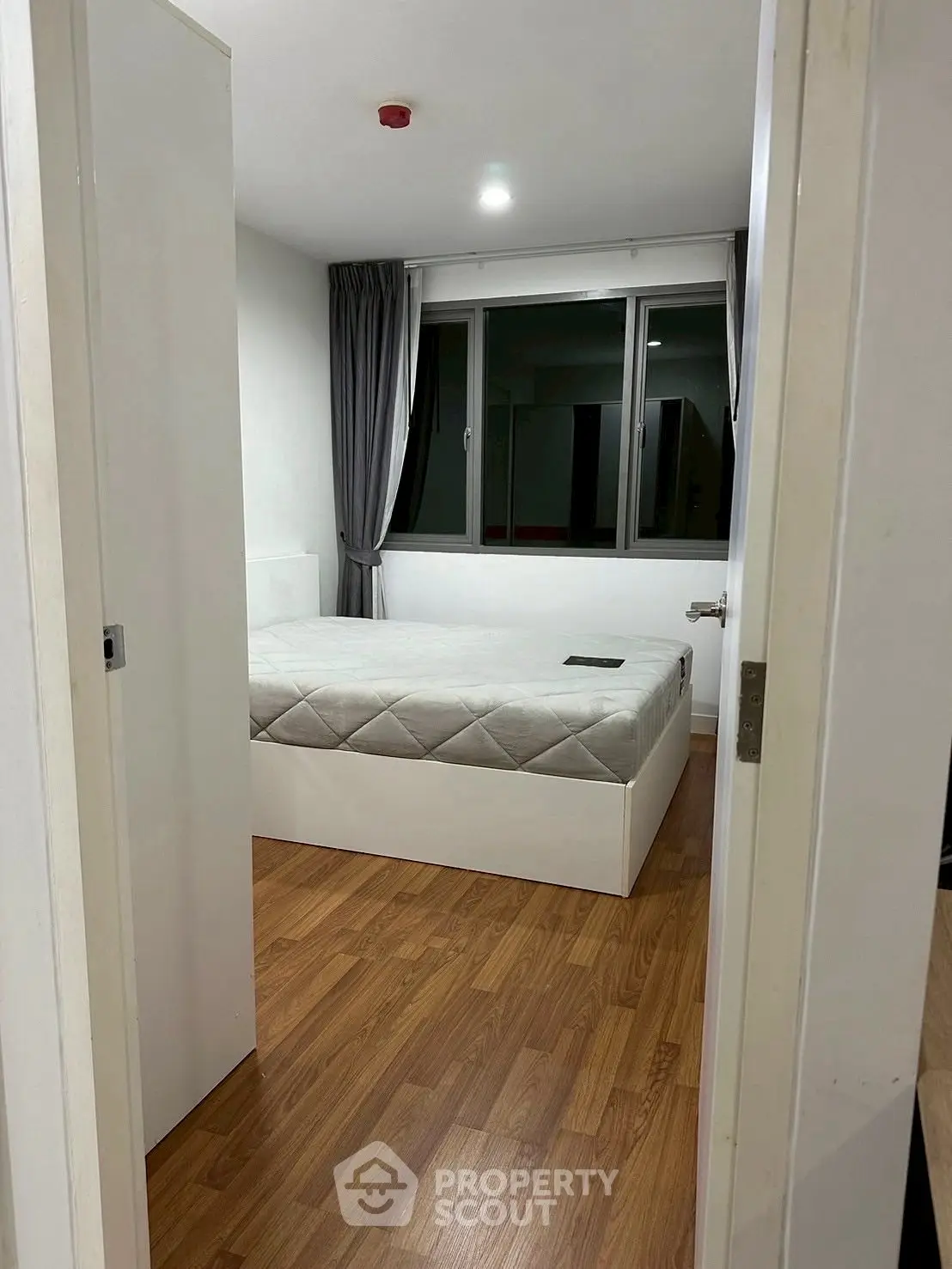 Modern bedroom with wooden flooring and large window, featuring a minimalist design.