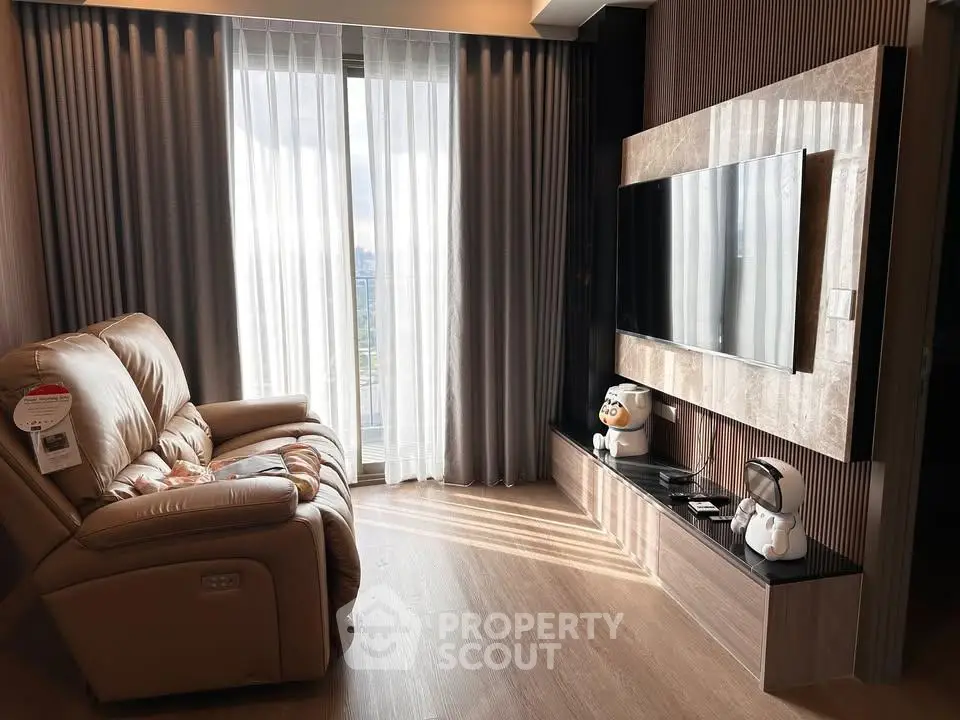Modern living room with large TV and comfortable recliner chair, featuring floor-to-ceiling windows.