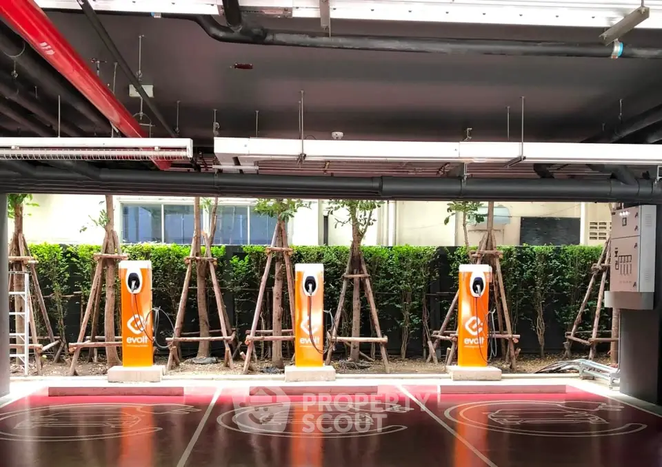 Modern parking area with electric vehicle charging stations and greenery backdrop.