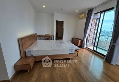 Spacious bedroom with wooden flooring and city view balcony in modern apartment.