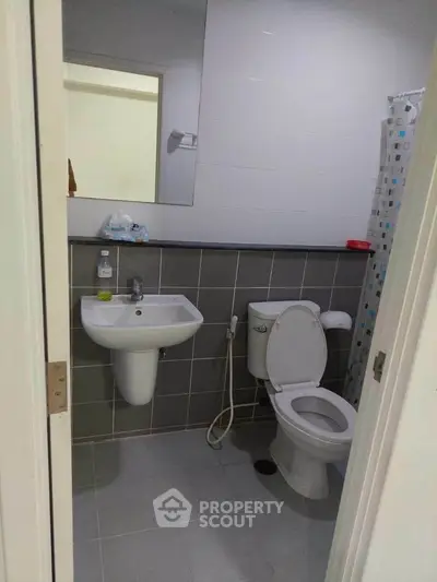 Modern bathroom with sleek fixtures and tiled walls, featuring a toilet, sink, and shower area.