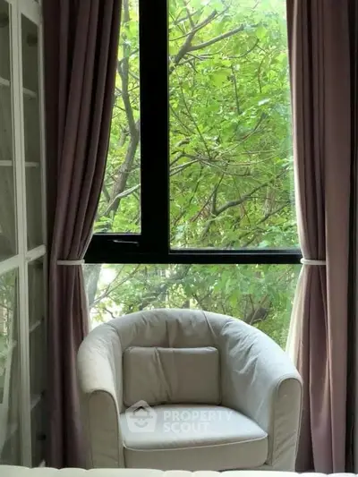 Cozy reading nook with plush armchair by a large window overlooking lush greenery.