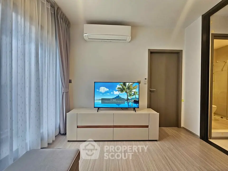 Modern living room with sleek furniture and air conditioning, featuring a flat-screen TV and elegant curtains.