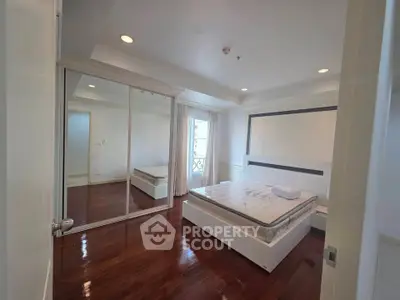 Spacious bedroom with elegant wooden flooring and large mirrored closet doors