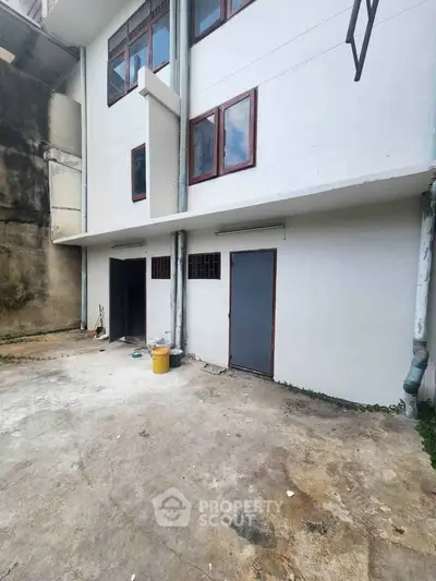 Exterior view of a building with white walls and multiple doors, showcasing potential for renovation.