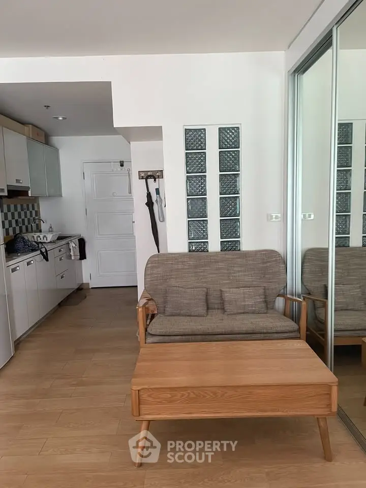 Charming compact living room with modern kitchen in open layout, featuring wooden flooring and stylish furniture.