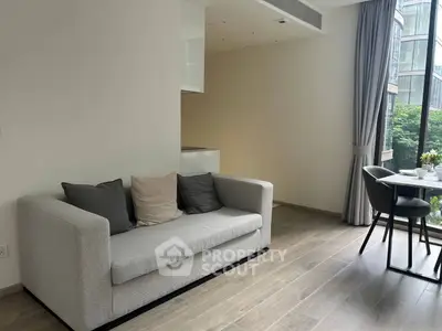 Modern living room with sleek sofa and dining area, large windows offering natural light.