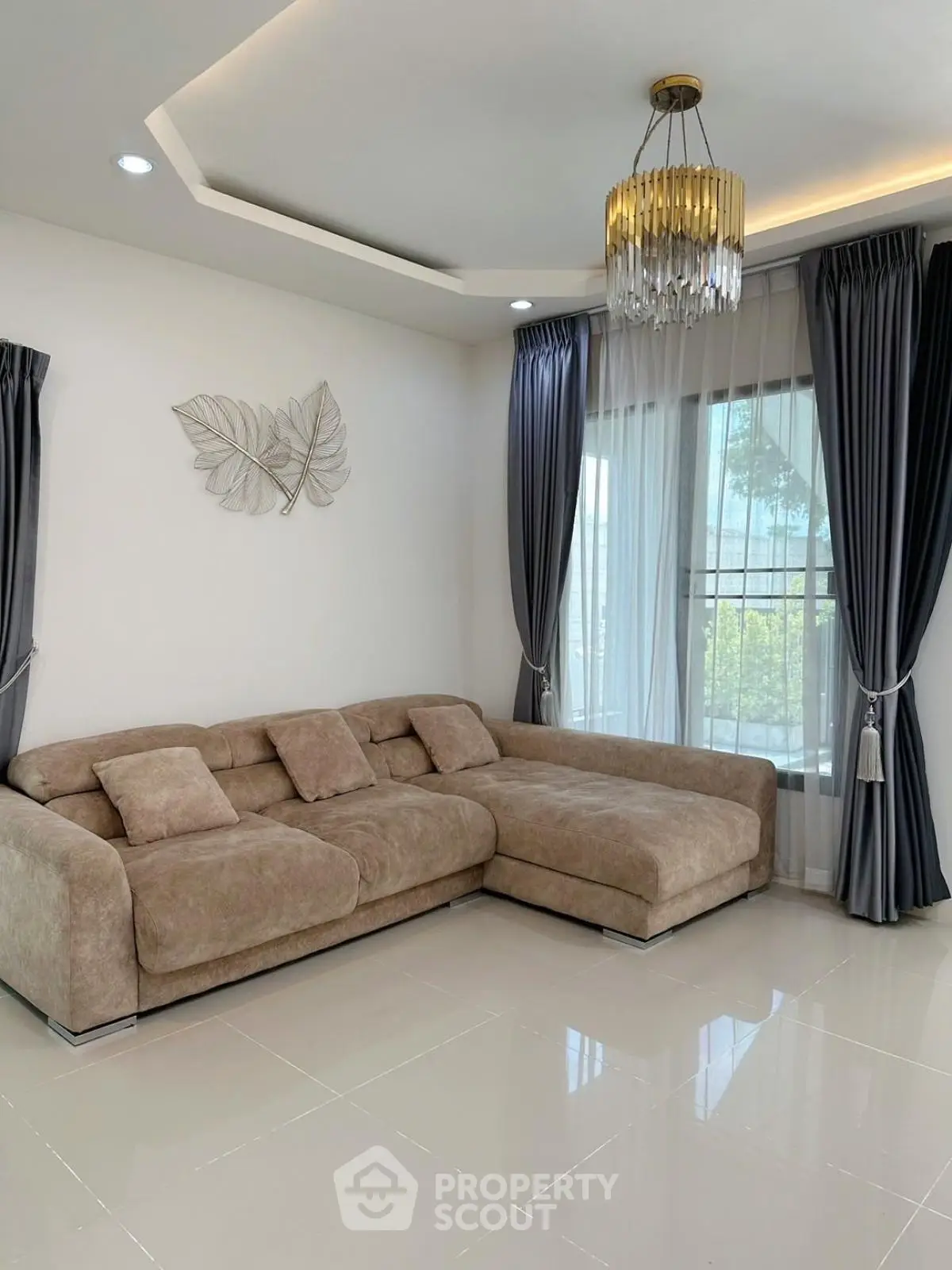 Elegant living room with plush sectional sofa and modern chandelier, featuring large windows and stylish curtains.