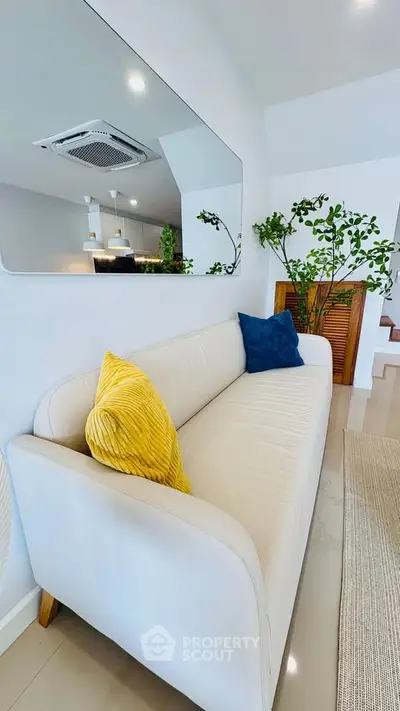 Modern living room with stylish sofa and vibrant cushions, featuring a sleek mirror and lush indoor plants.