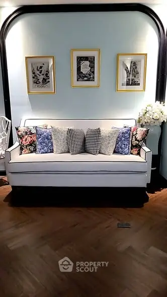 Elegant living room with stylish sofa and decorative pillows, framed art on pastel walls.