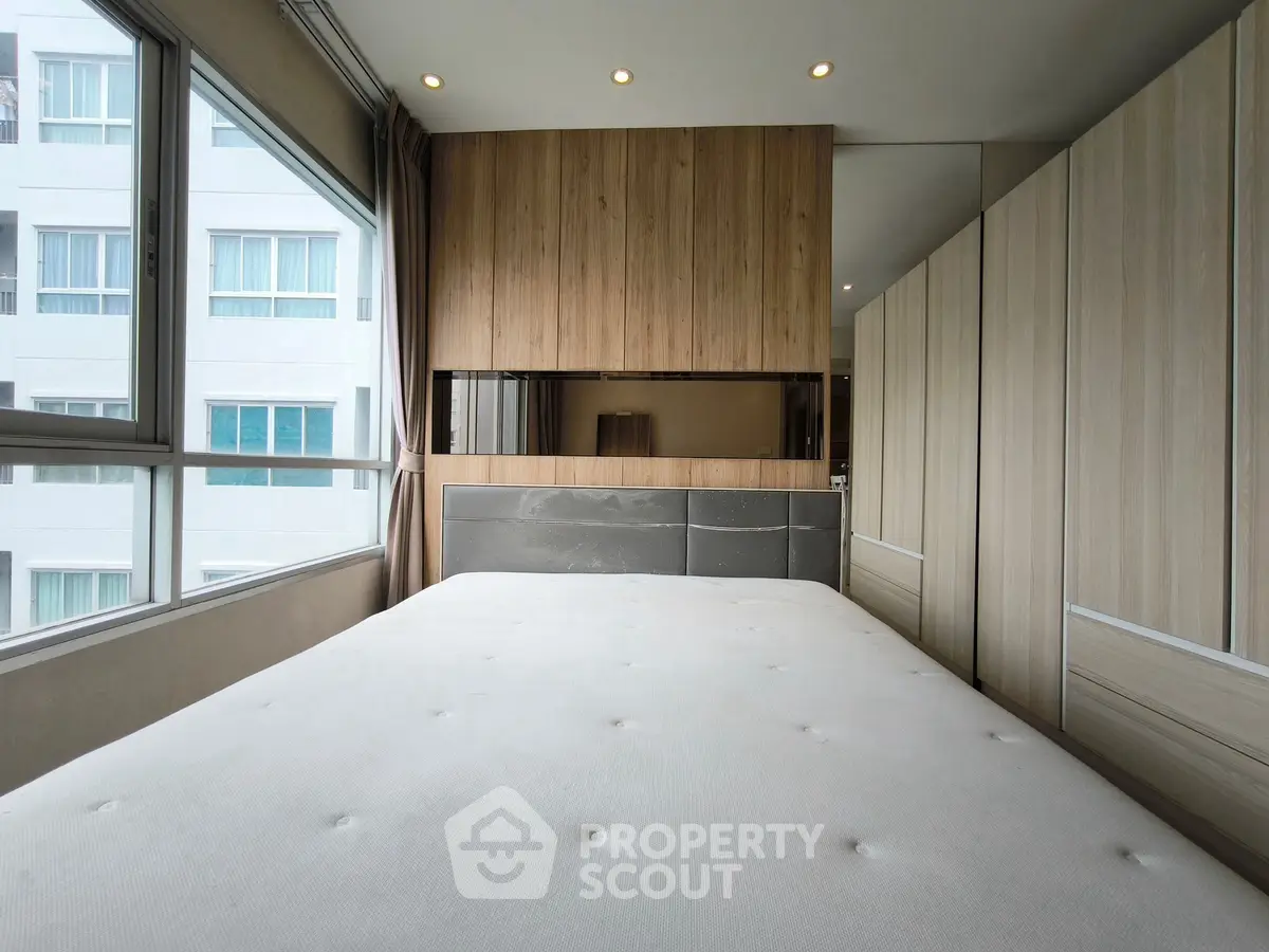 Modern bedroom with large windows and wooden accents in a high-rise apartment.