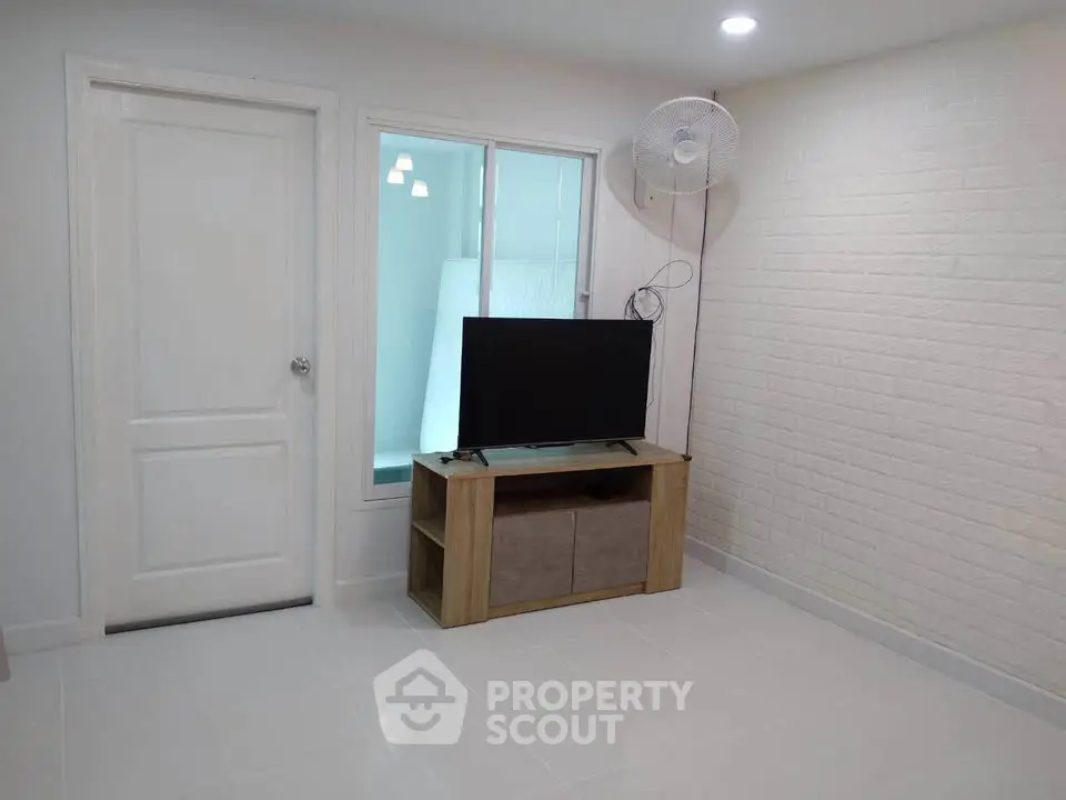 Modern living room with sleek TV stand and wall-mounted fan, featuring white brick accent wall.