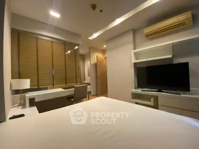 Modern bedroom with sleek design, featuring a TV, air conditioning, and a study area with a desk and chair.