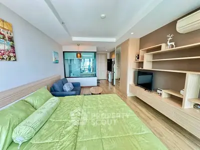Spacious modern bedroom with green bedding, cozy seating area, and stylish wooden shelving.