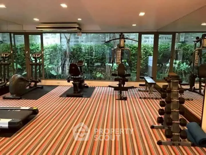 Spacious gym with modern equipment and large windows overlooking greenery.