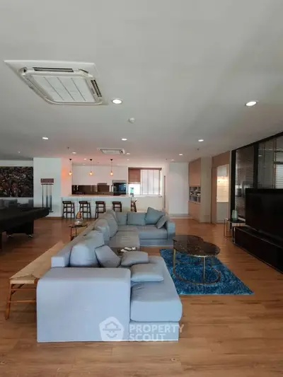 Spacious modern living room with open kitchen, featuring stylish furniture and wooden flooring.