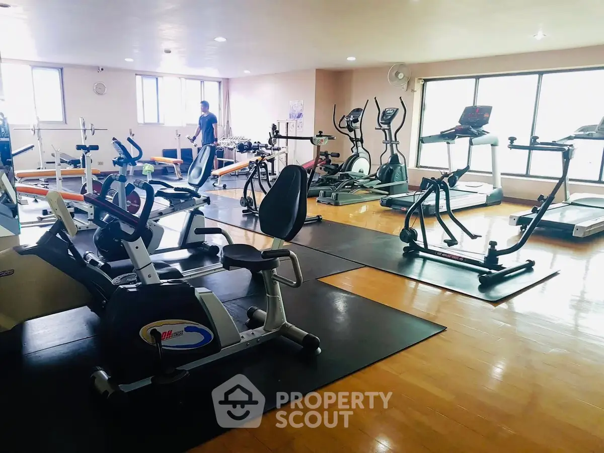 Spacious gym with modern fitness equipment and large windows for natural light.