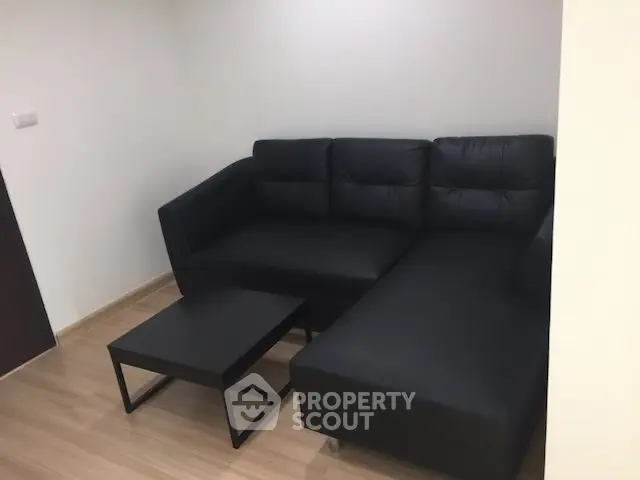 Modern living room with sleek black sofa and minimalist coffee table on wooden flooring.