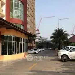 Modern building exterior with parking area and construction cranes in the background.
