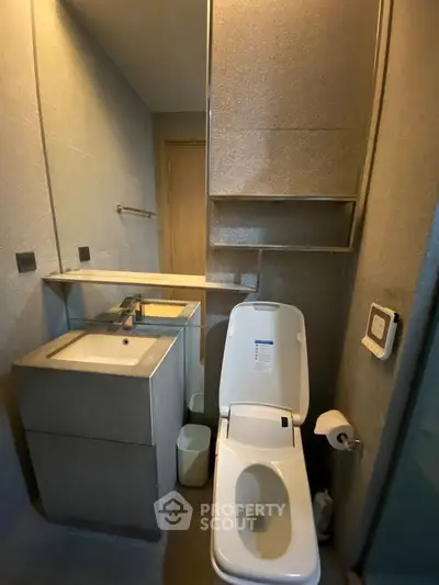 Modern bathroom with sleek fixtures and minimalist design, featuring a compact sink and toilet setup.