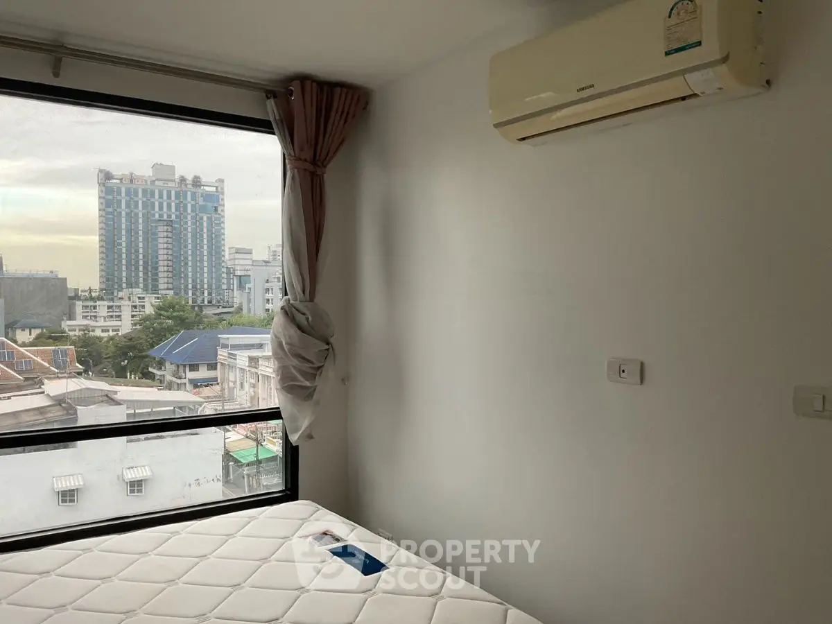 Modern bedroom with large window and city view, featuring air conditioning and minimalist decor.