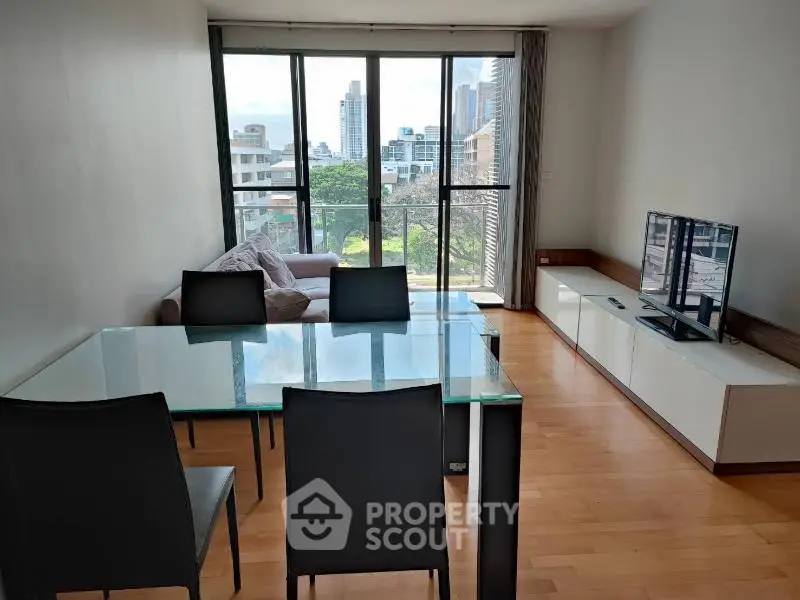 Modern living room with glass dining table and city view from large windows.