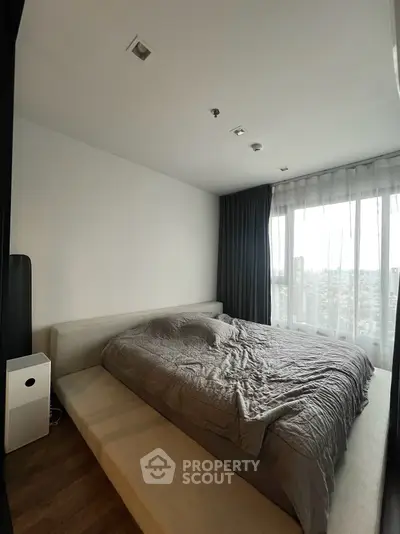 Spacious bedroom with large window offering city views, featuring a modern bed and sleek design.