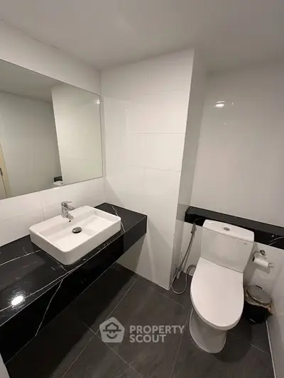 Modern bathroom with sleek black and white design, featuring a stylish sink and toilet.