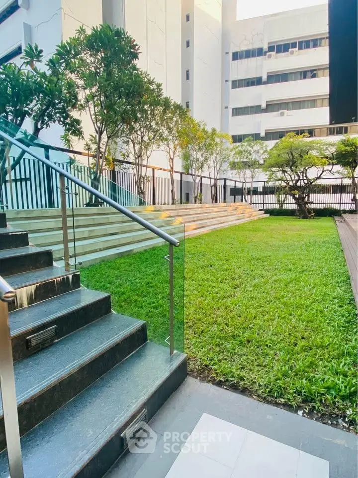 Charming urban garden with lush greenery and modern staircase in a residential complex.