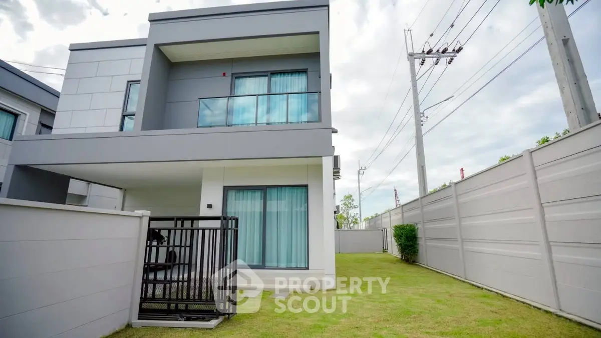 Modern two-story house with balcony and fenced yard in suburban setting.