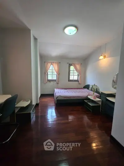 Cozy bedroom with wooden flooring and natural light from two windows.