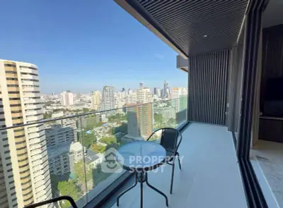 Stunning city view from a modern high-rise balcony with sleek glass railing and outdoor seating.