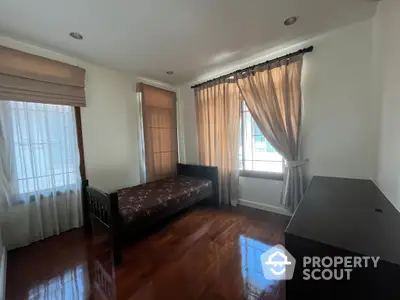 Spacious and sunlit living room with polished hardwood floors and large windows draped with elegant curtains, offering a comfortable and inviting atmosphere.