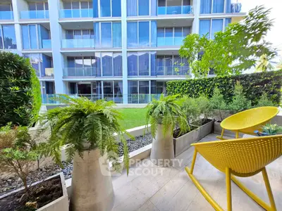Modern apartment building with lush garden and stylish yellow chairs on patio.