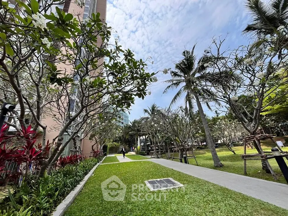 Lush garden pathway with tropical trees and manicured lawn in a residential complex.