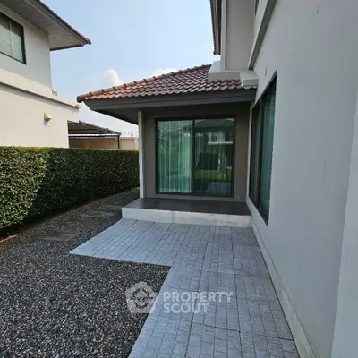 Modern house exterior with tiled patio and manicured hedge, showcasing sleek architectural design.