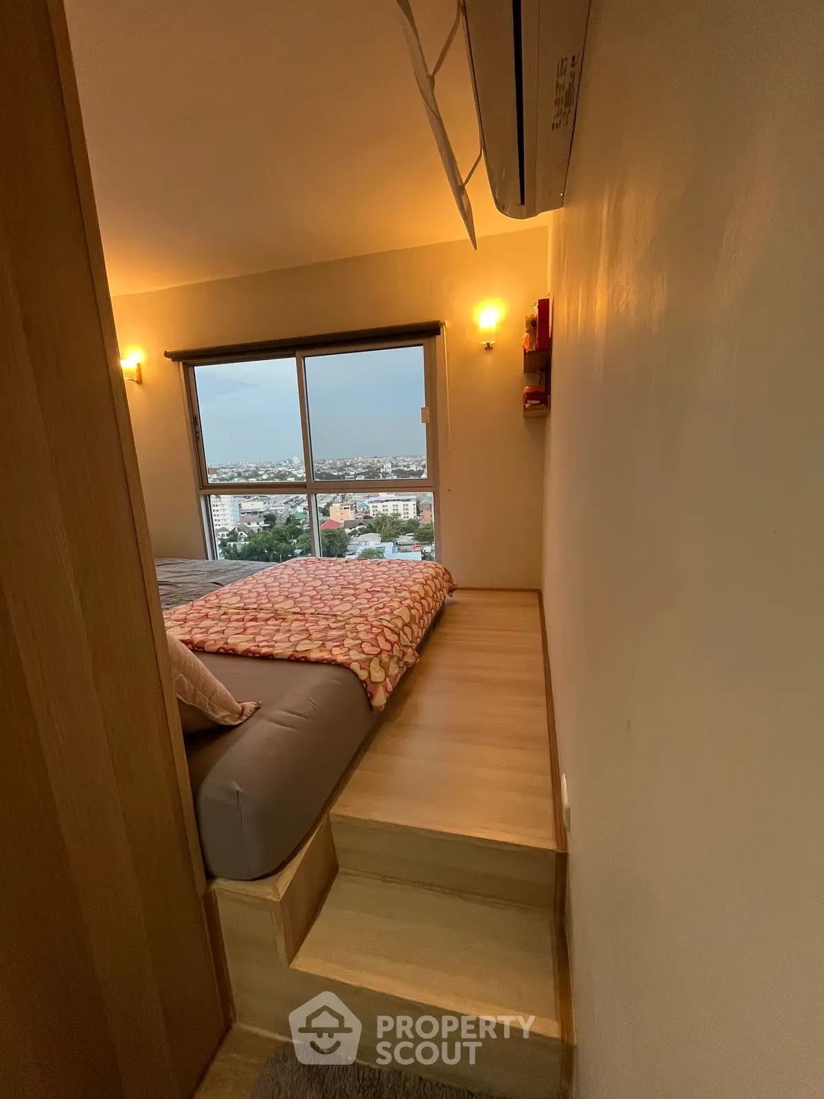 Cozy bedroom with elevated bed and panoramic city view from large window.