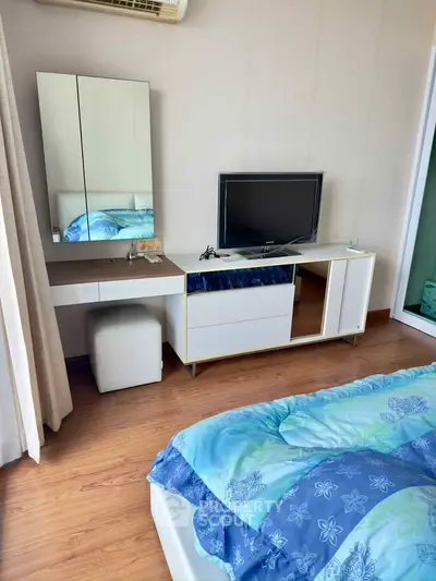 Cozy bedroom with modern furniture, featuring a TV and mirrored vanity, perfect for relaxation.