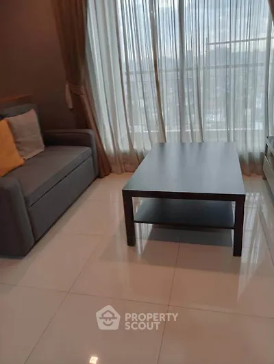 Modern living room with sleek sofa and coffee table, featuring floor-to-ceiling windows for natural light.